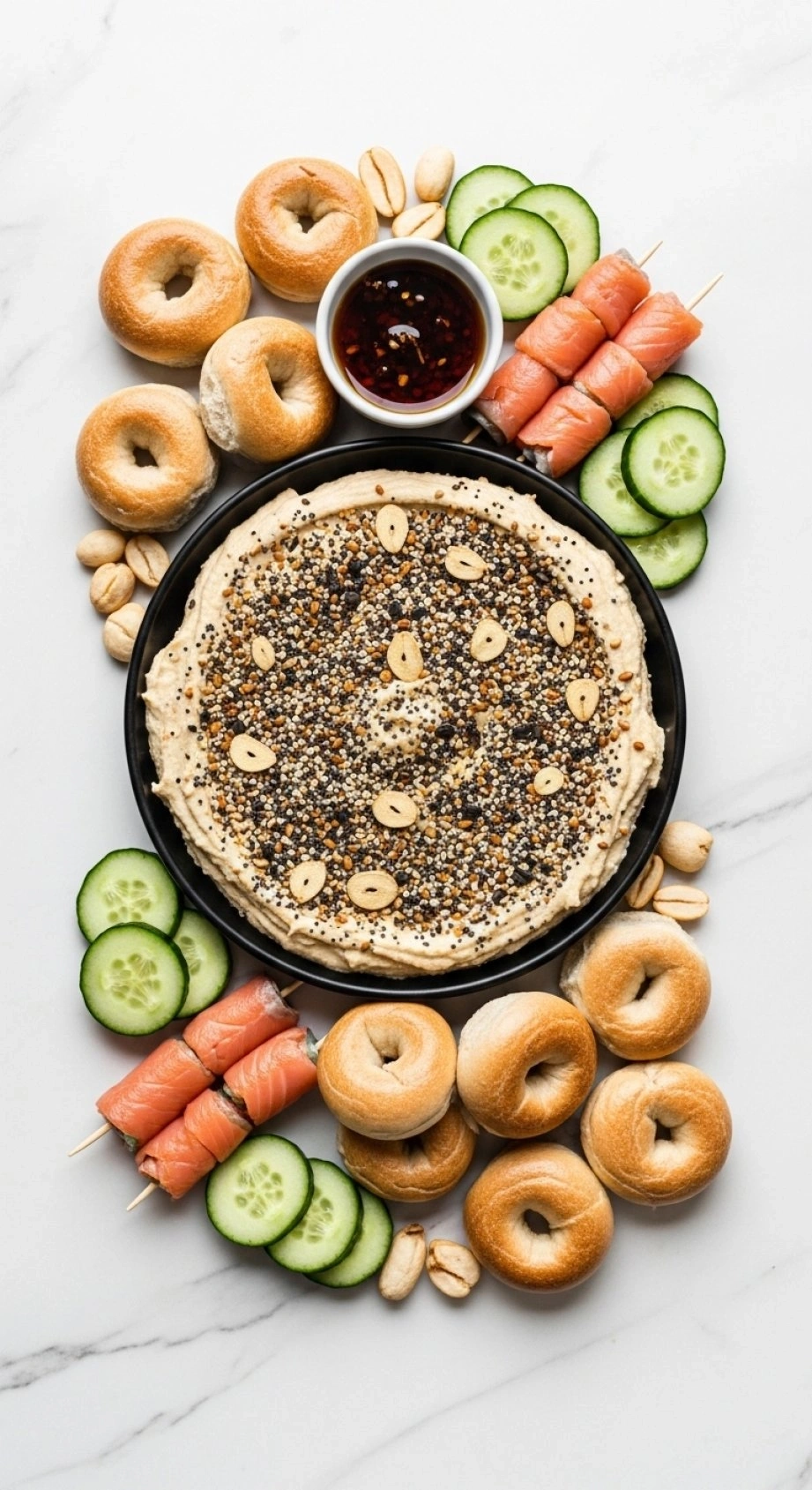 Everything Bagel Hummus With Seasoning, Mini Bagels, Cucumber Slices, And Smoked Salmon Rolls On Marble.