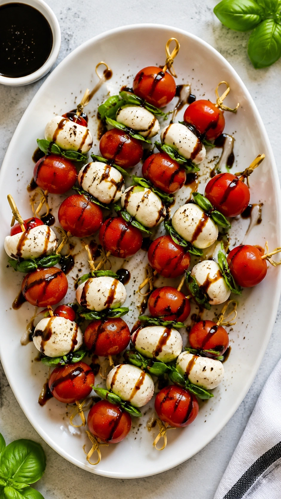 Elegant Caprese salad skewers with tomatoes, mozzarella, and basil drizzled with balsamic on a white platter.