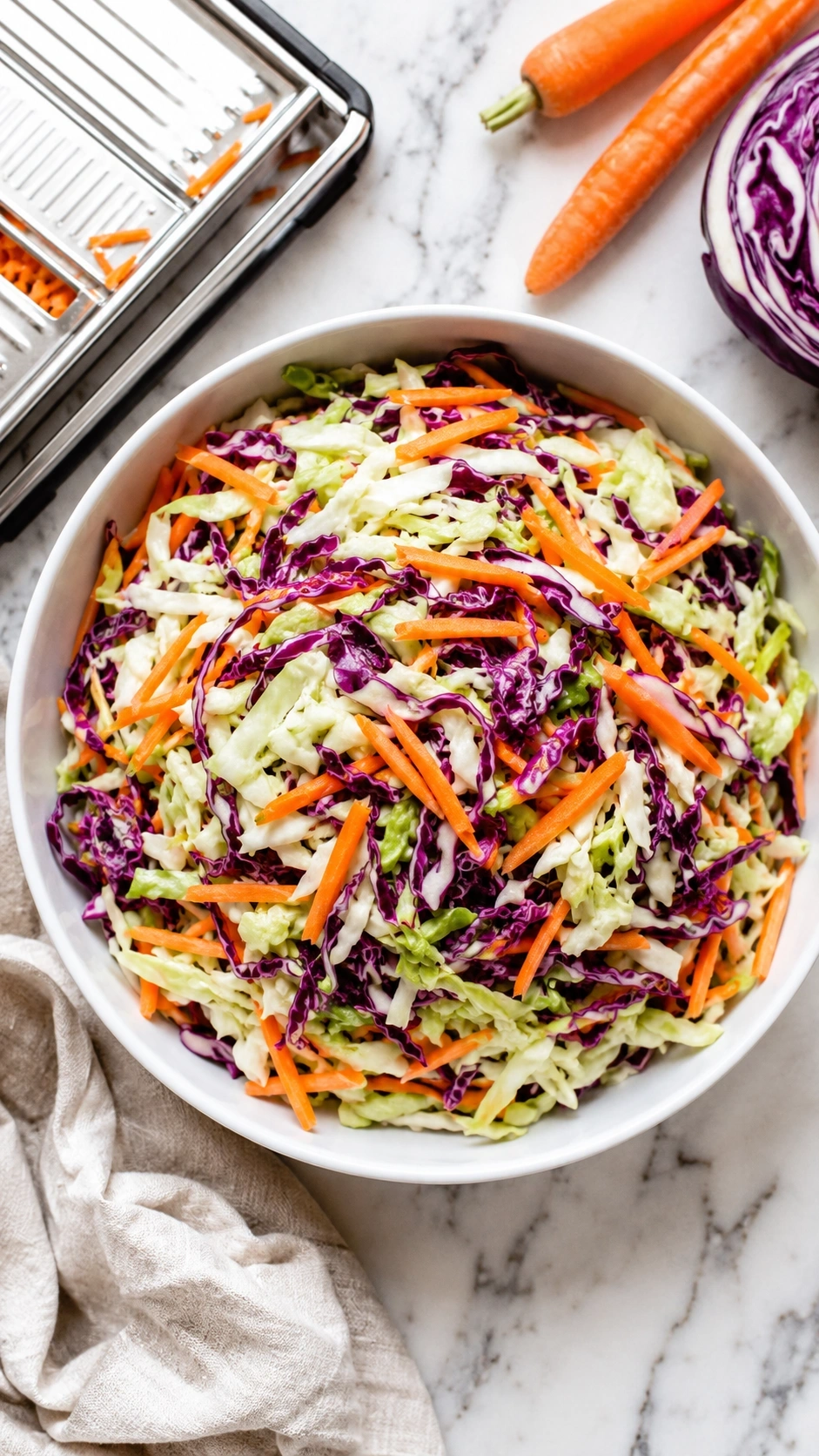 Top-down view of vibrant vinegar-based coleslaw with shredded cabbage, carrots, and vinaigrette on a marble countertop.