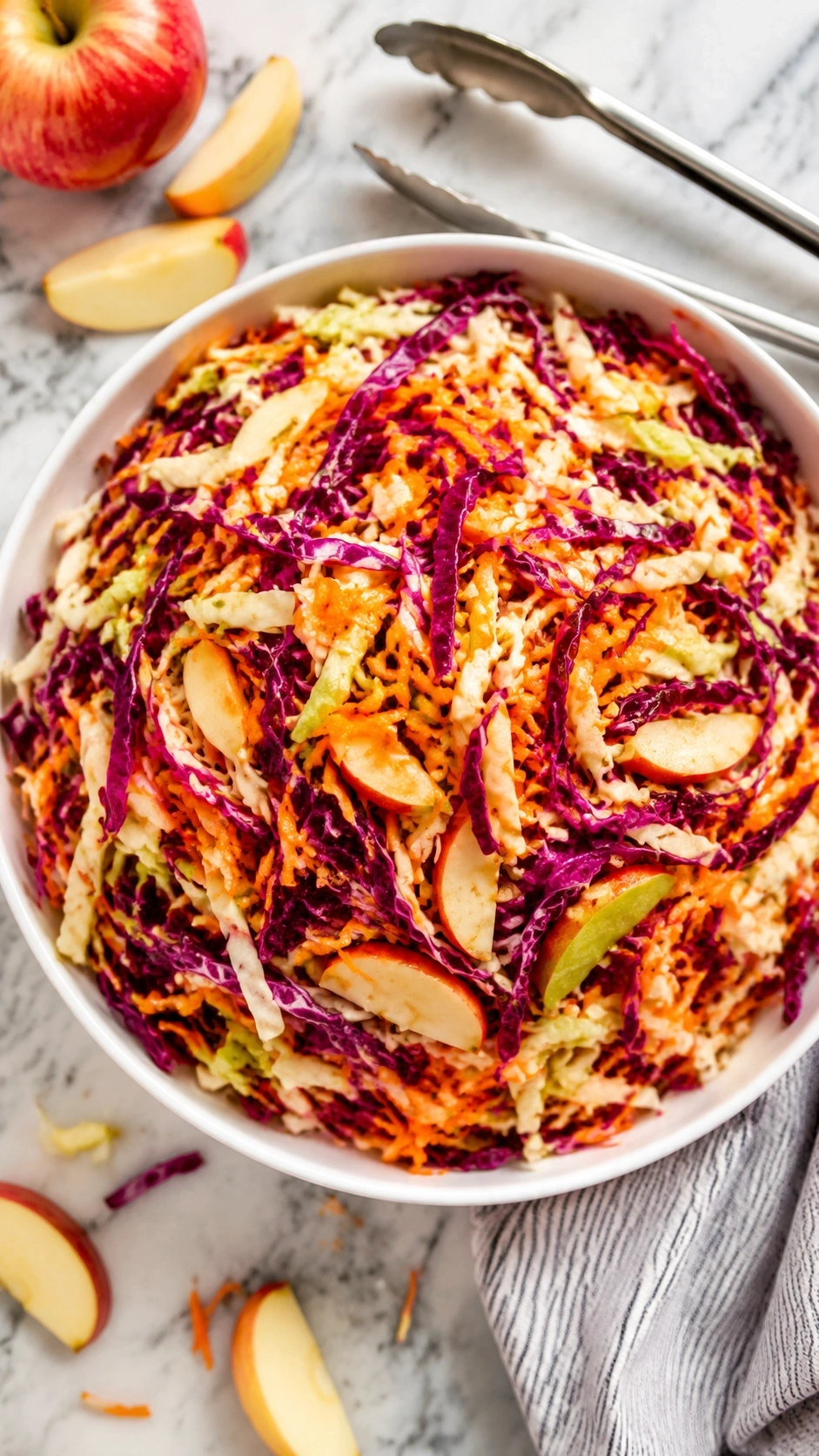 Vibrant apple cider vinegar coleslaw with purple cabbage, orange carrots, and green ribbons in a white bowl, served on marble.