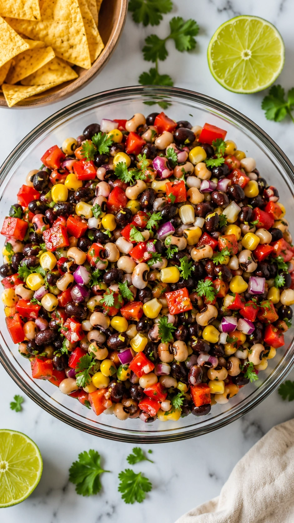 Fresh cowboy caviar bean salad with corn and peppers in a glass bowl on a marble counter with tortilla chips.