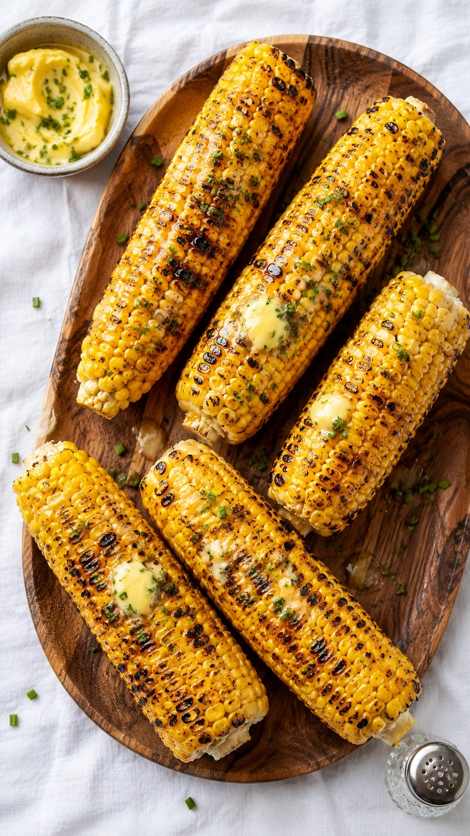 Grilled corn on the cob with honey butter and fresh chives served on a rustic wooden platter flat lay.
